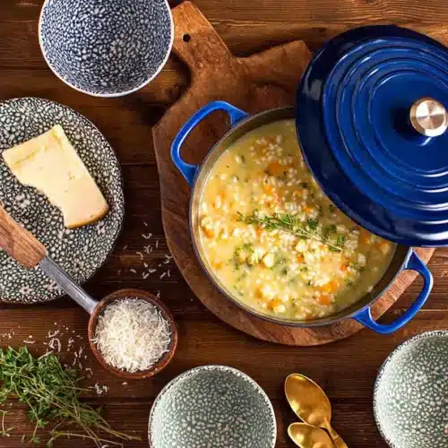 Creamy Italian chicken pastina soup in a blue pot with herbs and cheese on a wooden table