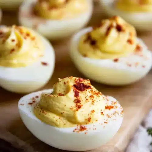 Creamy deviled eggs topped with paprika on a wooden board