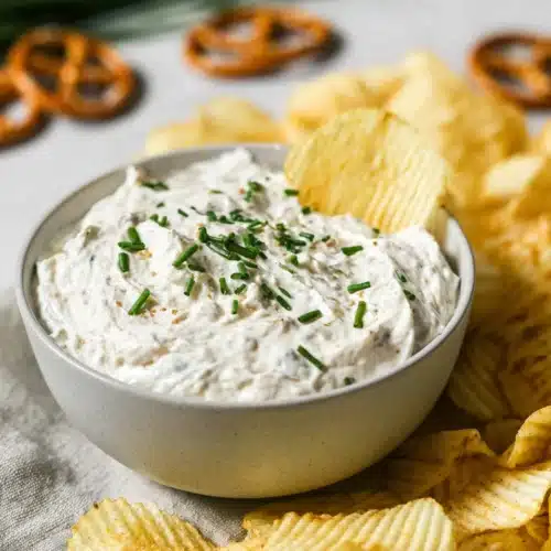 Creamy sour cream and onion dip with chives and potato chips in a bowl