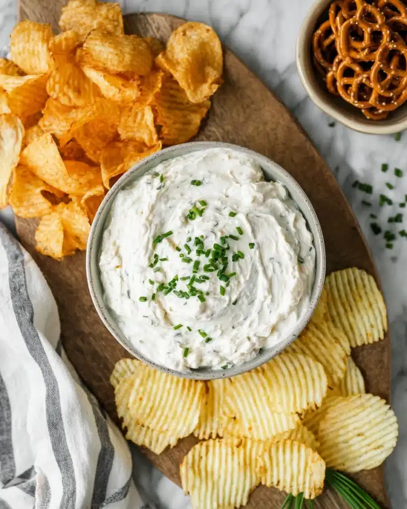 Sour cream and onion dip with chips and pretzels on a wooden board