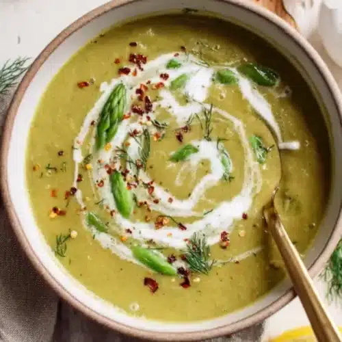 Creamy asparagus soup with dill and cream swirl in a white bowl