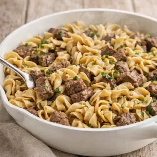 Beef tips and egg noodles in white skillet with parsley garnish