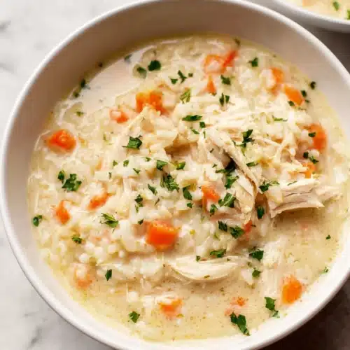 Creamy chicken and rice soup in a white bowl with carrots and parsley