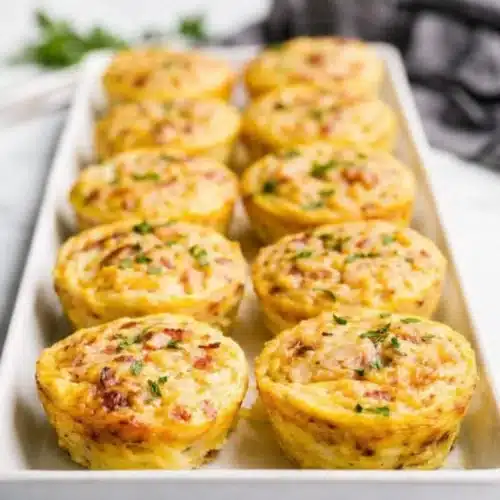 Golden cottage cheese egg bites with bacon and herbs in a white baking dish