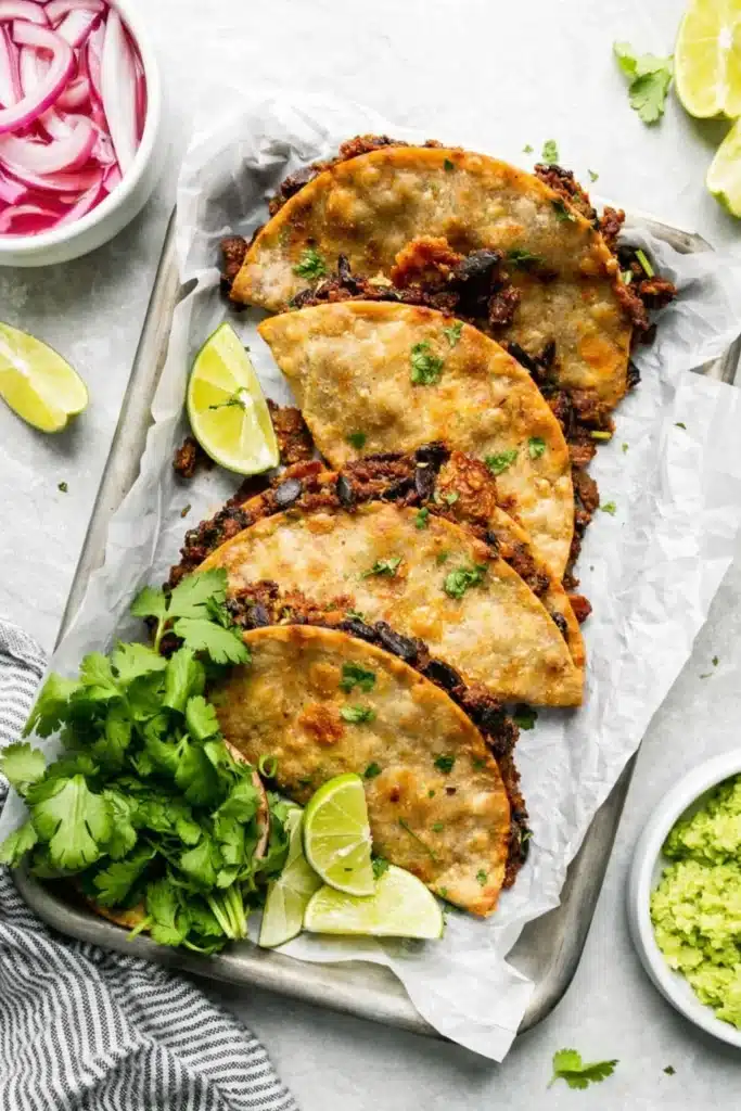 Crispy black bean tacos on tray with lime wedges and cilantro