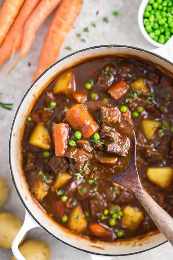 Ladle of Dutch oven beef stew with carrots, potatoes, and peas