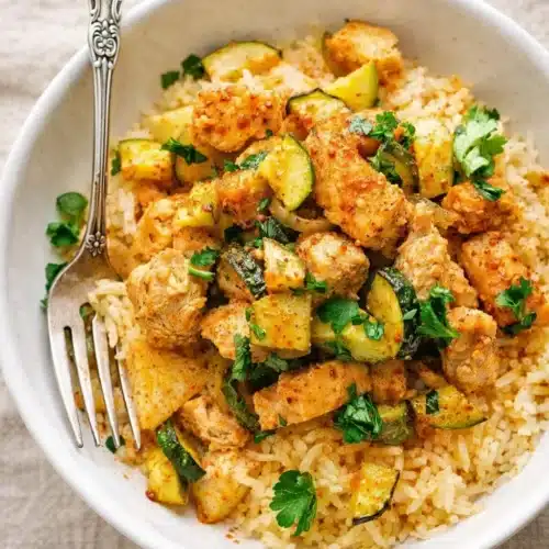 Easy baked chicken and zucchini served over rice in a white bowl with fresh herbs