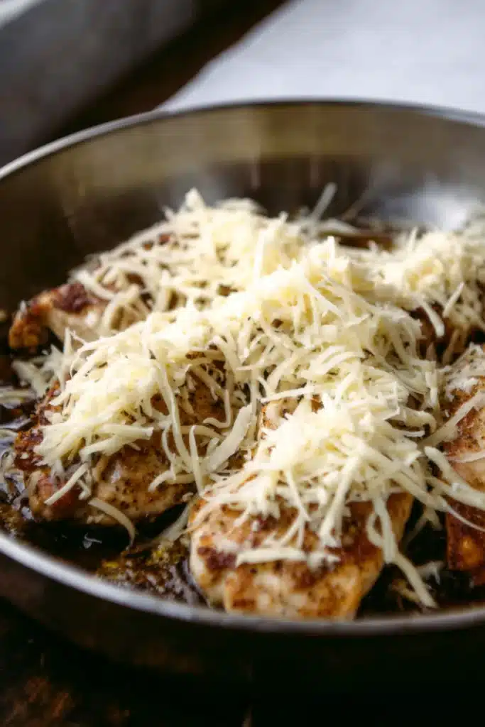 Chicken topped with shredded cheese in skillet before broiling for French Onion Chicken