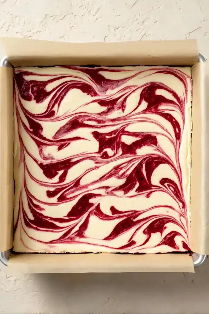 Raspberry swirl cheesecake brownie batter in baking pan
