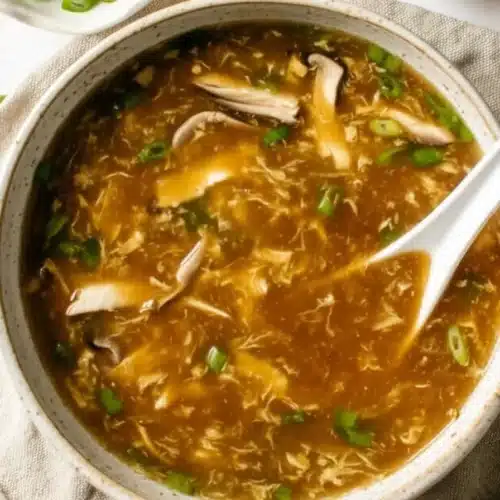 Hot and sour soup with mushrooms, tofu, and scallions in a white bowl