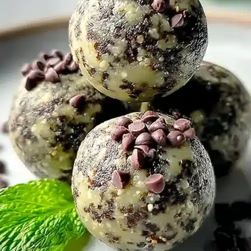 Mint chocolate chip protein balls stacked on a plate with chocolate chips and mint leaves