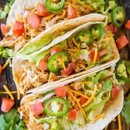 Slow cooker queso chicken tacos with lettuce, cheese, tomatoes, and jalapeños