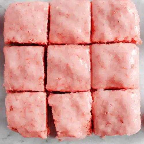 Strawberry Brownies Recipe with pink glaze cut into squares on a marble board