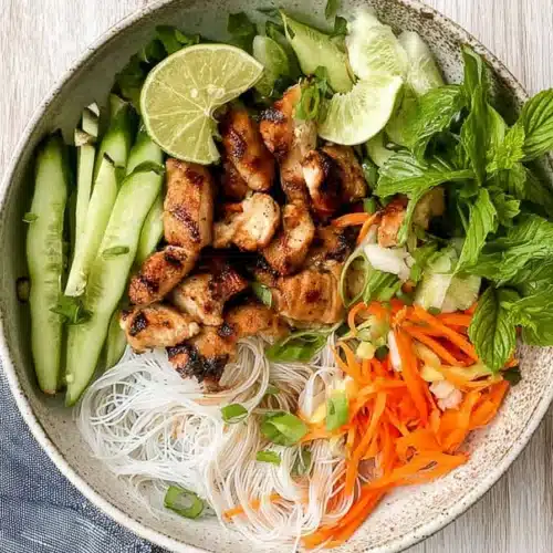 Vietnamese noodle bowl with grilled chicken, rice noodles, carrots, cucumbers, and herbs