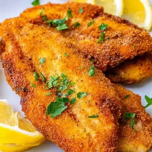 Crispy golden air fryer catfish fillets with lemon wedges on a white plate