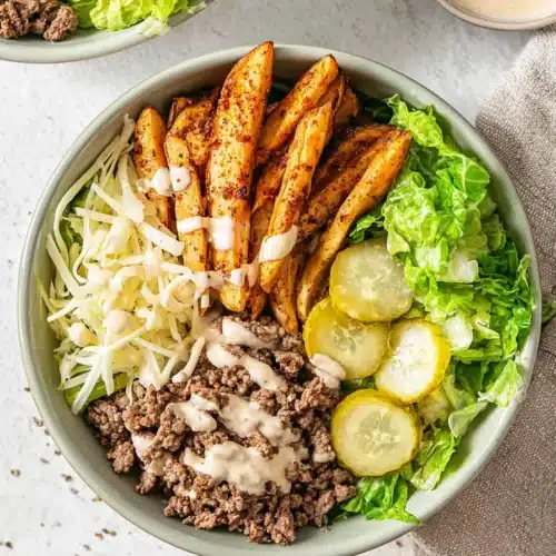 Burger bowl with crispy potatoes, ground beef, lettuce, pickles, and creamy sauce