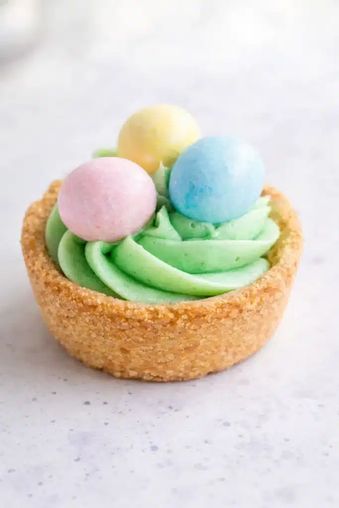 Close-up Easter Basket Sugar Cookie Cups with green frosting and pastel candy eggs