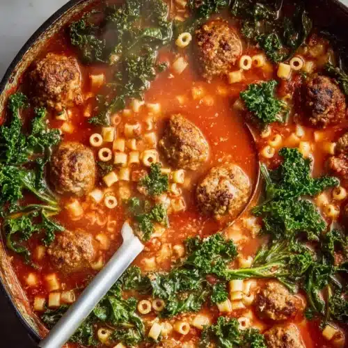 Hearty Italian meatball soup with kale, pasta, and tomato broth in a rustic pot