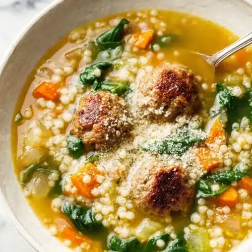Italian wedding soup with meatballs, spinach, and pearl pasta in golden broth