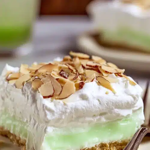 Slice of pistachio lush dessert with whipped topping and toasted almonds on white plate