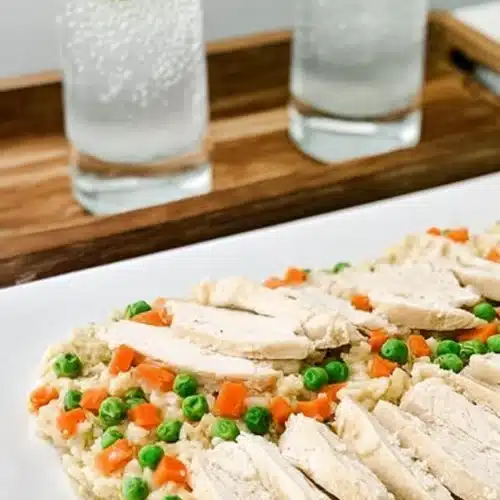 Slow cooker chicken and rice with sliced chicken, peas, and carrots on a white plate