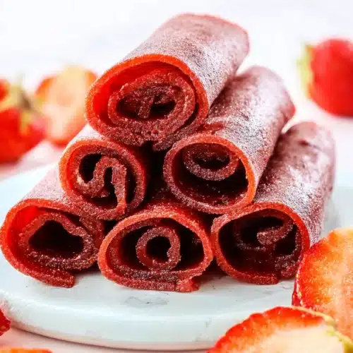 Homemade strawberry fruit roll-ups stacked with fresh strawberries on a light plate
