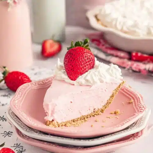 Slice of Strawberry Jello Cream Pie with whipped cream and fresh strawberry on a pink plate