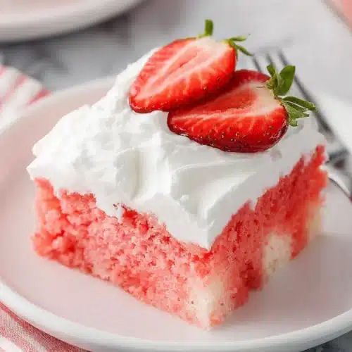 Moist strawberry Jello poke cake slice with whipped topping and fresh strawberries