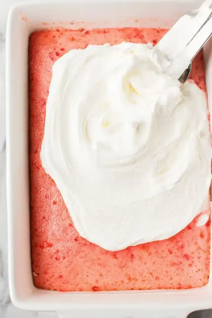 Spreading whipped topping on strawberry Jello poke cake