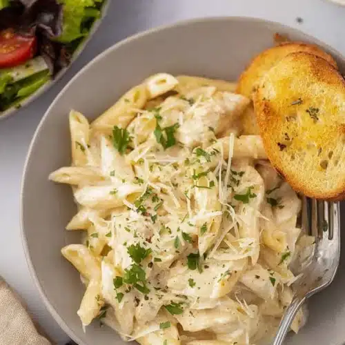 Creamy chicken Alfredo penne pasta with parmesan and garlic toast on rustic table
