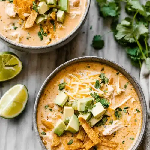 Creamy white chicken chili with avocado, cheese, and tortilla strips in bowls on a marble surface