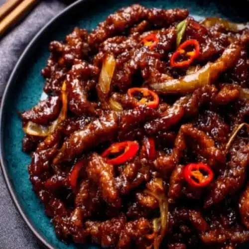 Crispy chilli beef on blue plate with glossy sweet-spicy sauce and red chillies