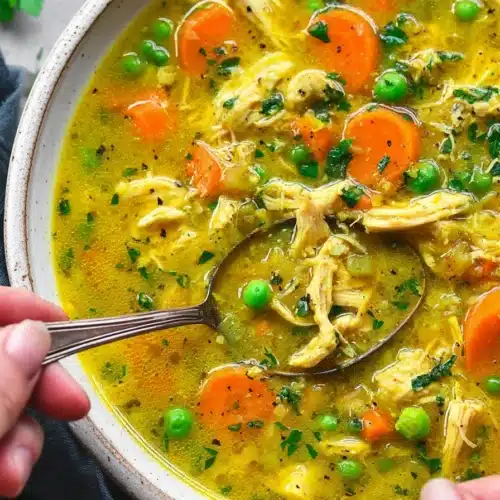 Anti inflammatory turmeric chicken soup with shredded chicken, carrots, peas, and golden broth