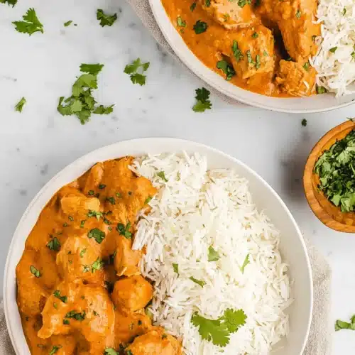 Butter chicken slow cooker with rice and cilantro in white bowls