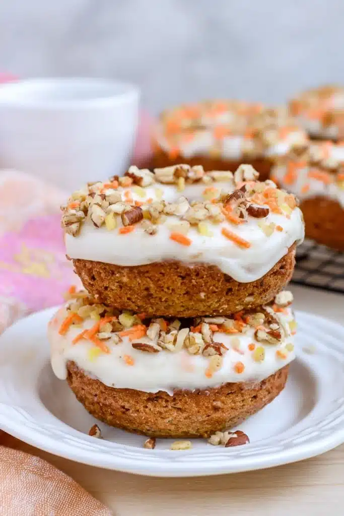 Carrot Cake Donuts That Are Soft, Spiced, and Perfect for Easter 1 Stacked carrot cake donuts with cream cheese frosting, chopped nuts, and orange sprinkles on a white plate