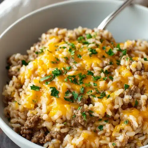 Cheesy ground beef and rice casserole in a bowl with melted cheddar and parsley garnish