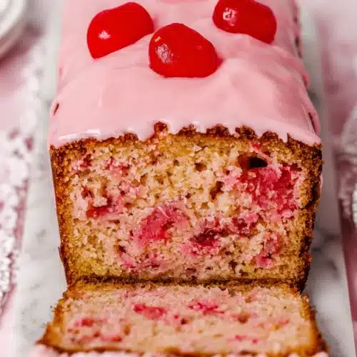 Cherry bread loaf with pink glaze and maraschino cherries on top, sliced to show moist crumb