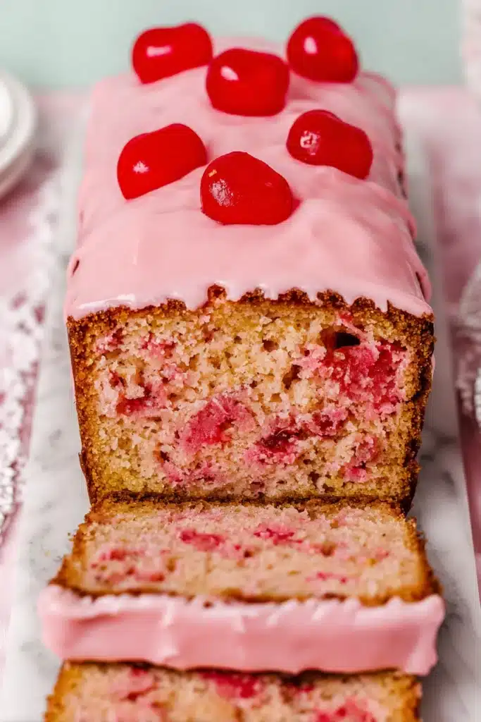 Cherry bread loaf with pink glaze and maraschino cherries on top, sliced to show moist crumb