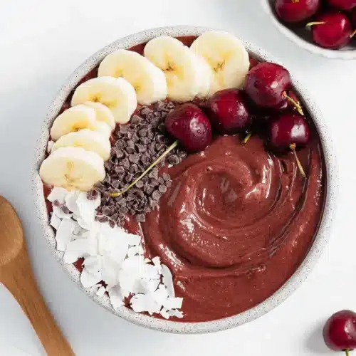 Chocolate cherry smoothie bowl with banana slices, coconut flakes and fresh cherries