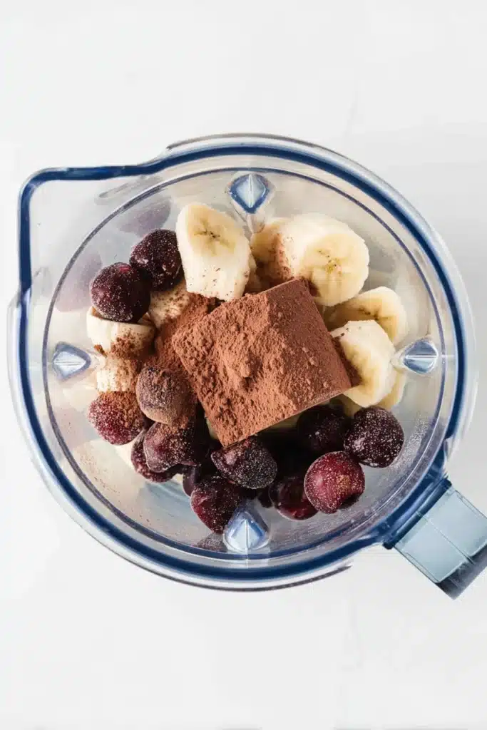 Blender with frozen banana, cherries, and cocoa powder for chocolate cherry smoothie bowl