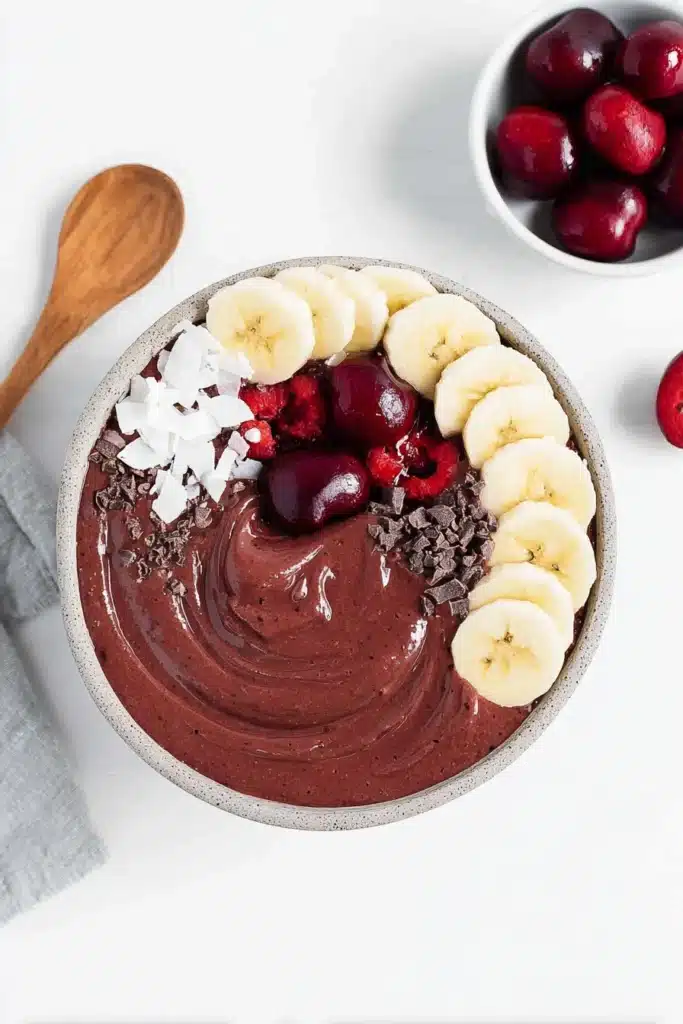 Chocolate cherry smoothie bowl with banana slices, coconut flakes and fresh cherries
