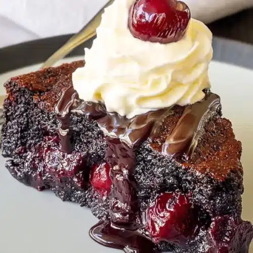 Slice of chocolate cherry upside down cake with whipped cream and chocolate drizzle