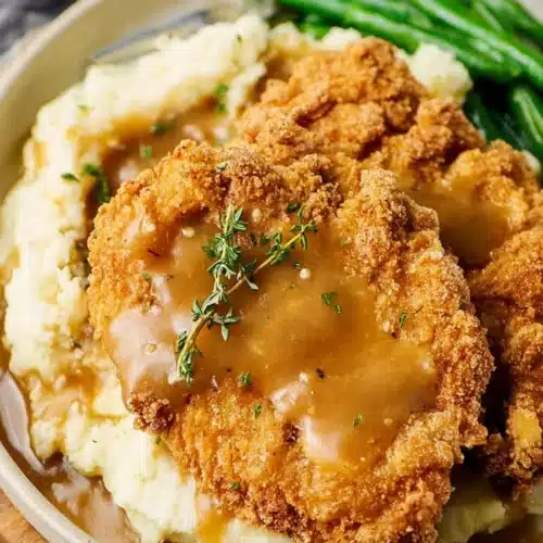 Country fried chicken with mashed potatoes and brown gravy on white plate