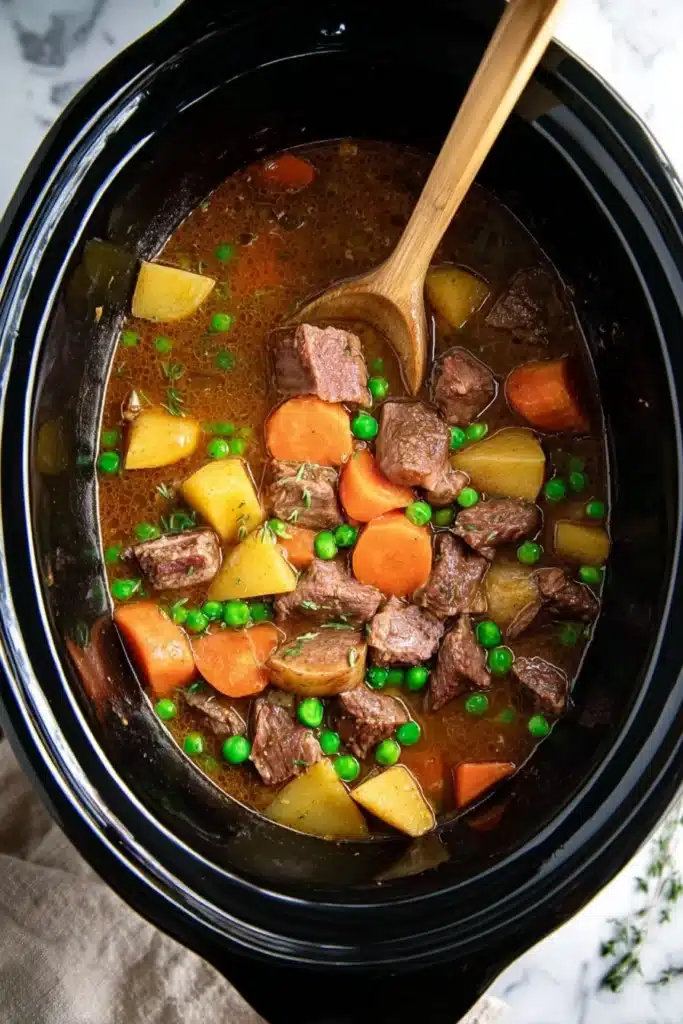 Crockpot beef stew with beef, carrots, potatoes, and peas in slow cooker