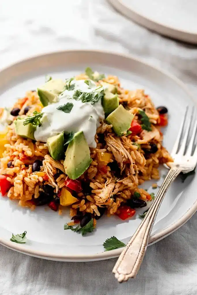 Easy Chicken Burrito Casserole 1 Easy chicken burrito casserole with avocado, black beans, and sour cream on ceramic plate
