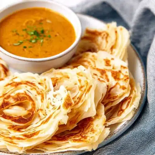 Flaky roti canai with curry on plate, crispy layered flatbread breakfast