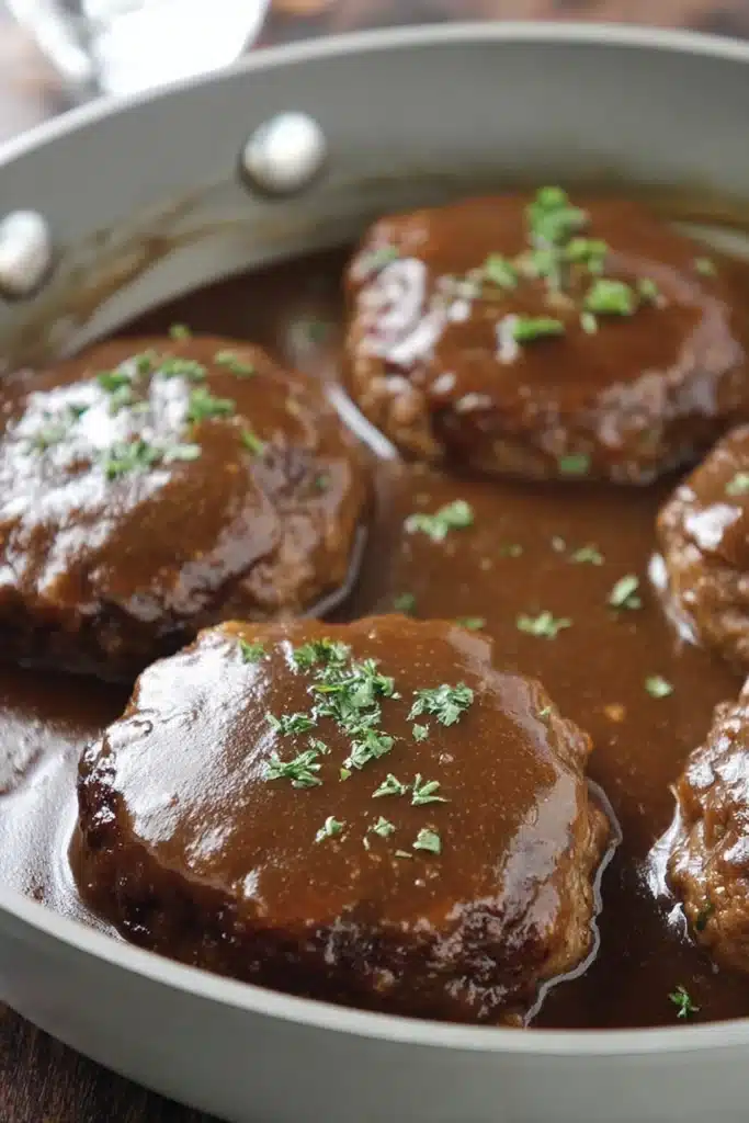Simple Salisbury Steak Easy and Juicy Family Dinner 2 Simple Salisbury steak patties simmering in brown gravy in skillet