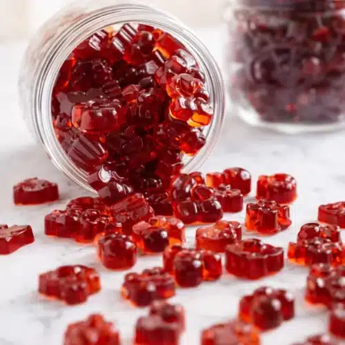 Homemade tart cherry gummies spilling from a glass jar on a light surface
