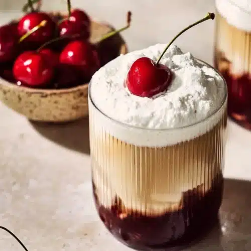 Viral Cherry Vanilla Latte That Tastes Amazing and Easy 4 Iced cherry vanilla latte with whipped foam and fresh cherry garnish in layered glass
