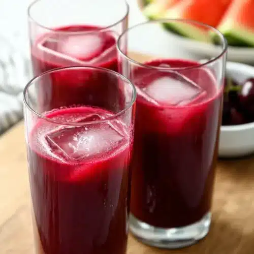 Three glasses of watermelon cherry beet juice with ice on marble surface